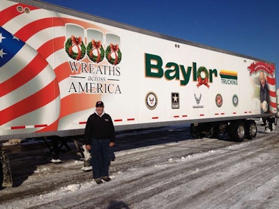 Baylor Trucking’s founder, Robert Baylor stands by a trailer that was used to deliver wreaths to military cemeteries.