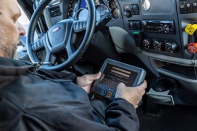 Man using an Omnitracs ELD in the cabin of a semi-truck