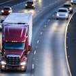Dark red big rig semi truck transporting cargo in refrigerator semitrailer running on the wide multilines highway at night with turned on headlights