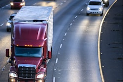 Dark red big rig semi truck transporting cargo in refrigerator semitrailer running on the wide multilines highway at night with turned on headlights