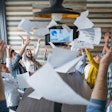 People sitting around desk throwing paper in the air