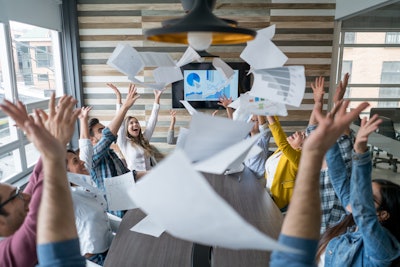 People sitting around desk throwing paper in the air