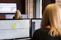 woman working desk with two monitors looking at data