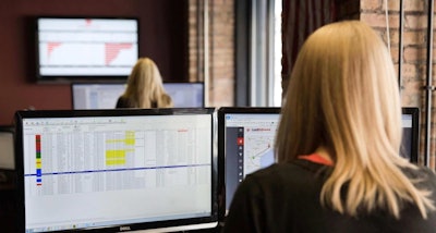 woman working desk with two monitors looking at data