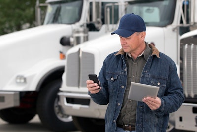 Man holding a tablet and checking his phone in front of parked semi-trucks