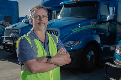 Man with arms crossed in front of parked semi trucks