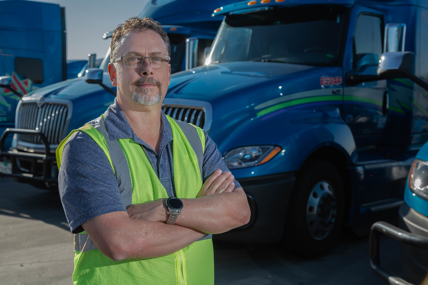 Man with arms crossed in front of parked semi trucks