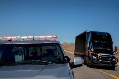 Police car with alert lights on with semi truck to the side on the highway