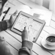 man looking on ipad with cup of coffee on table next to him