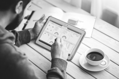 man looking on ipad with cup of coffee on table next to him