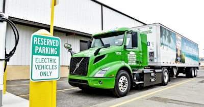Green Volvo VNR Electric truck with corona beer trailer parked in a reserved parking spot