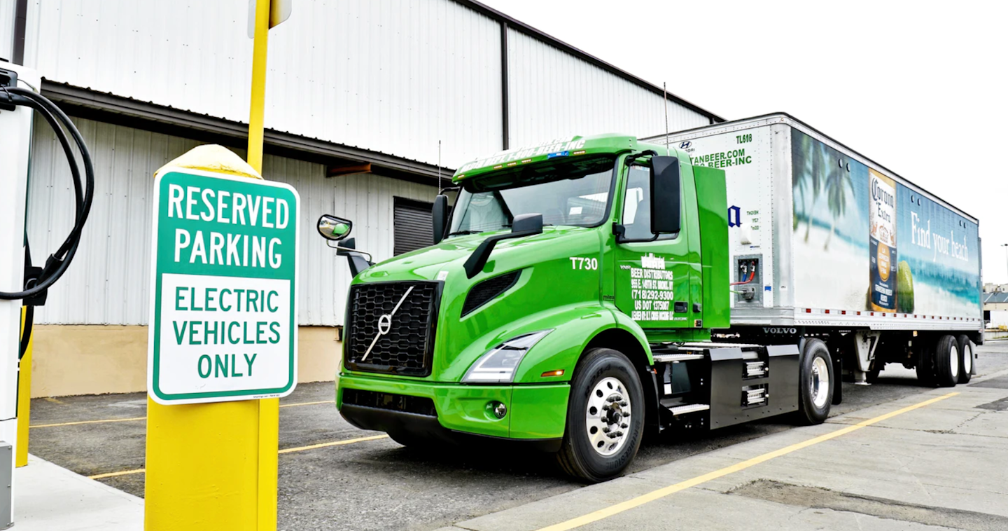 Green Volvo VNR Electric truck with corona beer trailer parked in a reserved parking spot