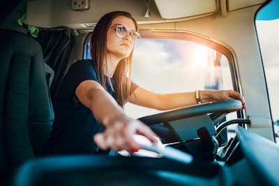 A young, female driver behind the wheel of a truck.