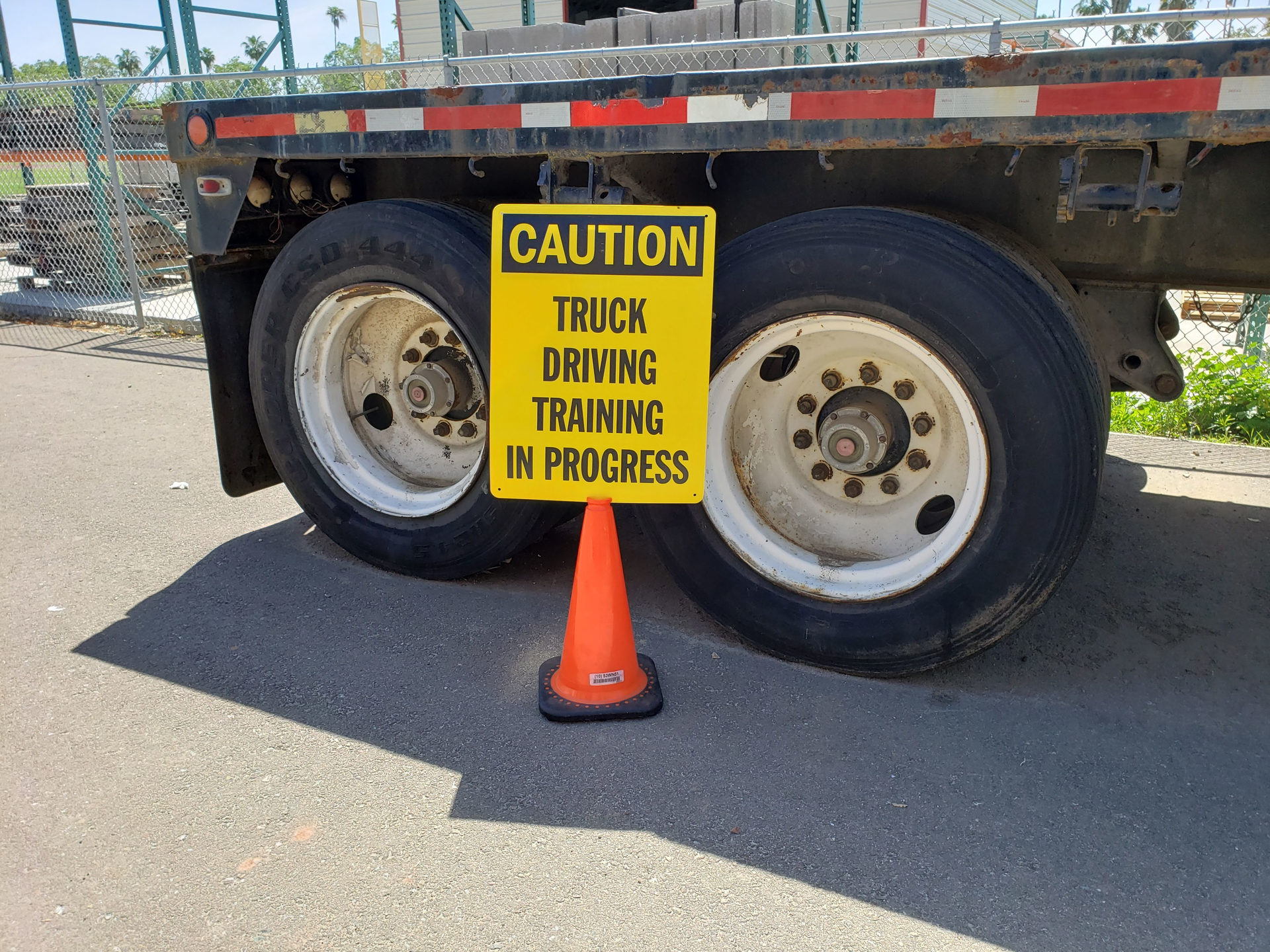 caution truck driving training in progress sign in front of the back wheels of a semi-truck