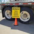 caution truck driving training in progress sign in front of the back wheels of a semi-truck