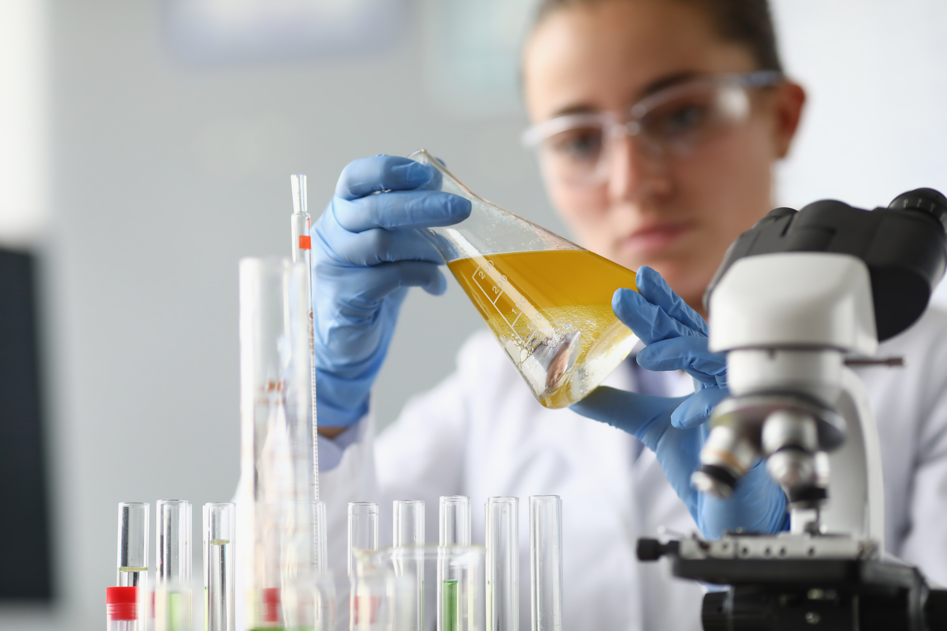 lab technician looking at a sample of yellow-tinted fluid in a laboratory flask