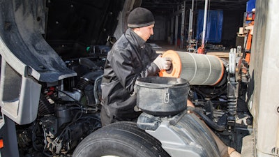 Technician replacing filter on heavy-duty truck.