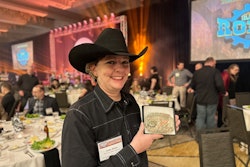 A woman in a black shirt and black cowboy hat holds up a belt buckle.