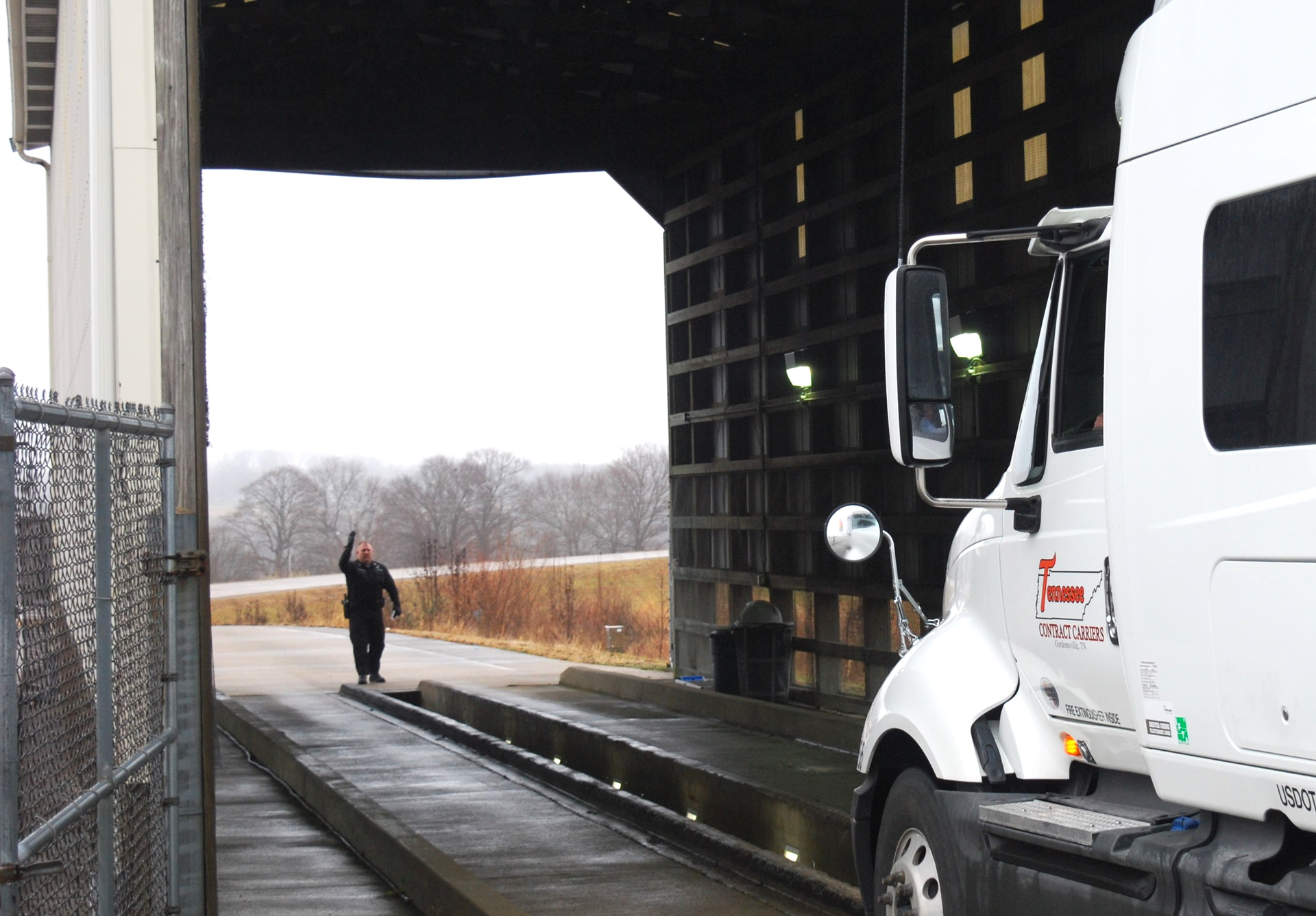 Semi-truck entering an inspection barn with an officer at the opposite end directing the driver