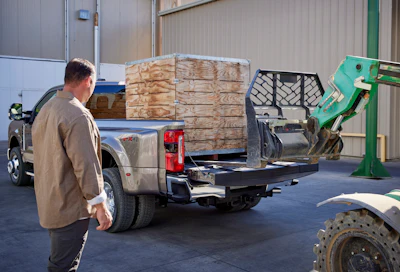 silver 2023 Ford Super-Duty F-350 Lariat being loaded by green telehandler with wooden box in bed