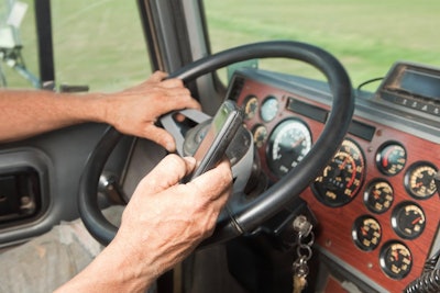 Trucker holding cellphone while behind the wheel of a semitruck