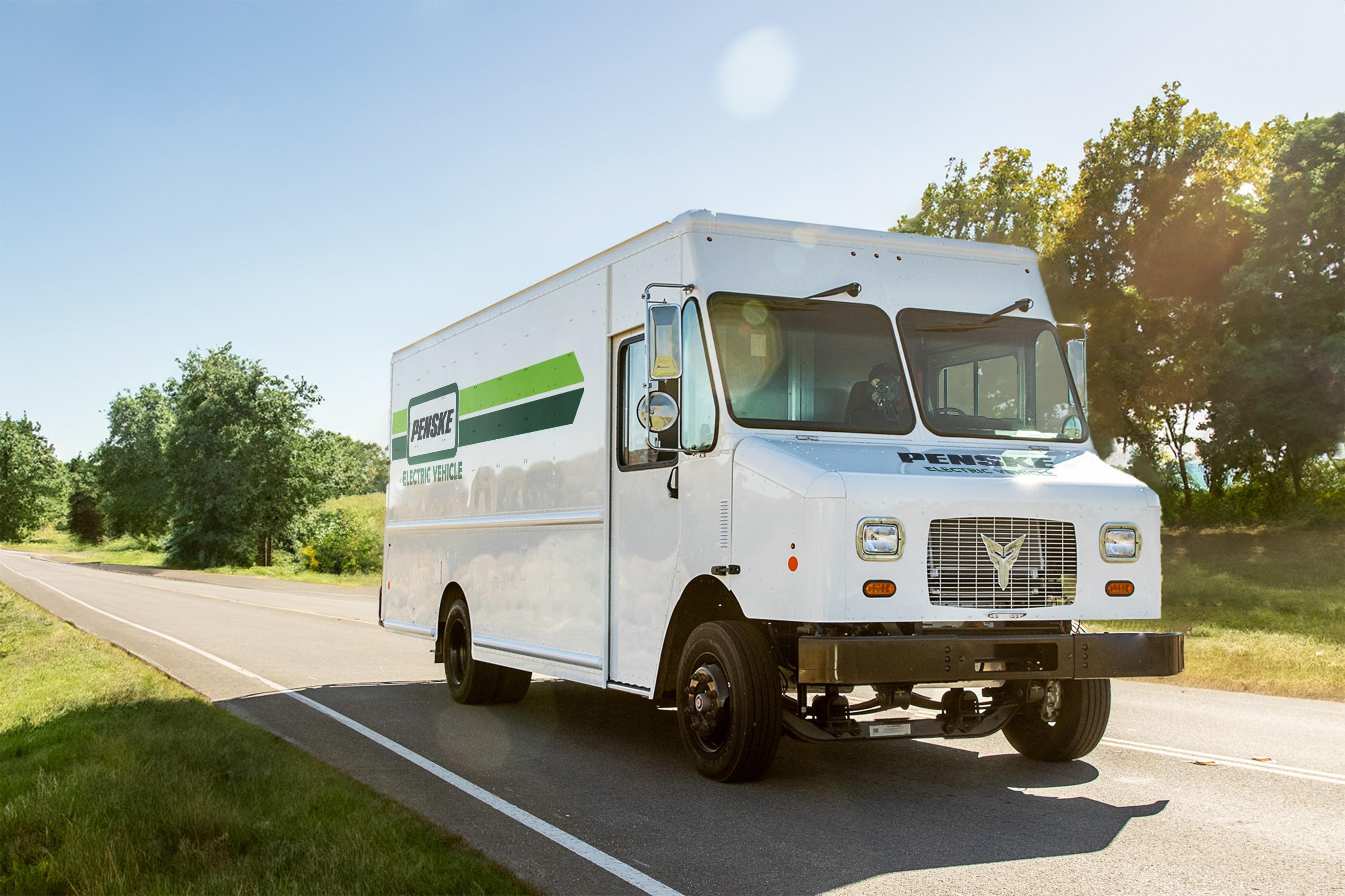 An Xos Stepvan in Penske livery driving down a road.