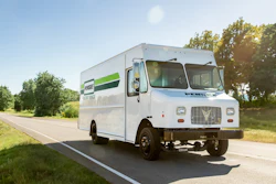 An Xos Stepvan in Penske livery driving down a road.