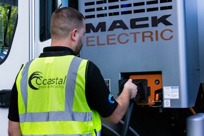 A man plugs in a Mack Electric refuse truck for charging.