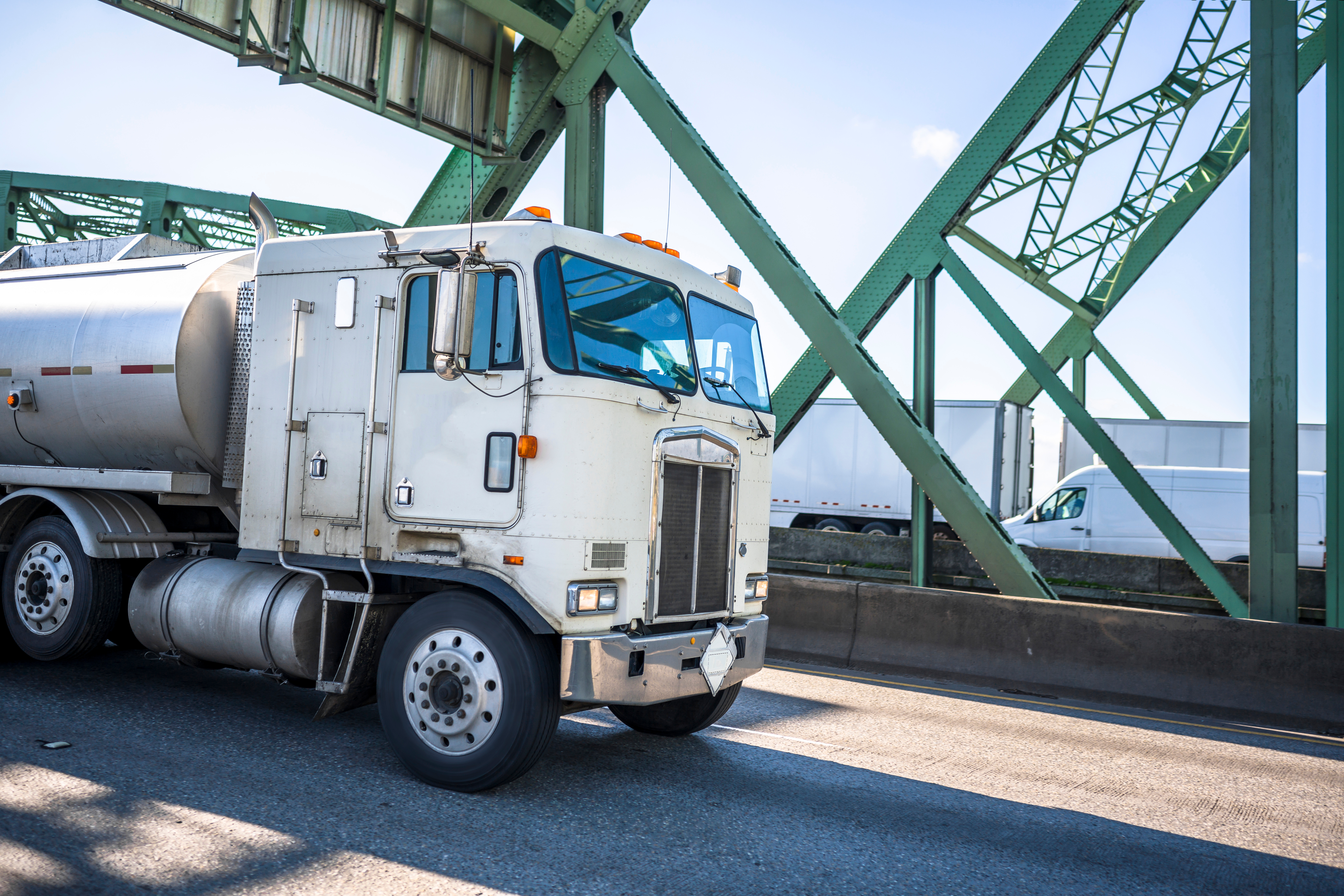 Old fashioned cab over big rig semi truck transporting fuel in tank semi trailer running on the truss arched Interstate Bridge