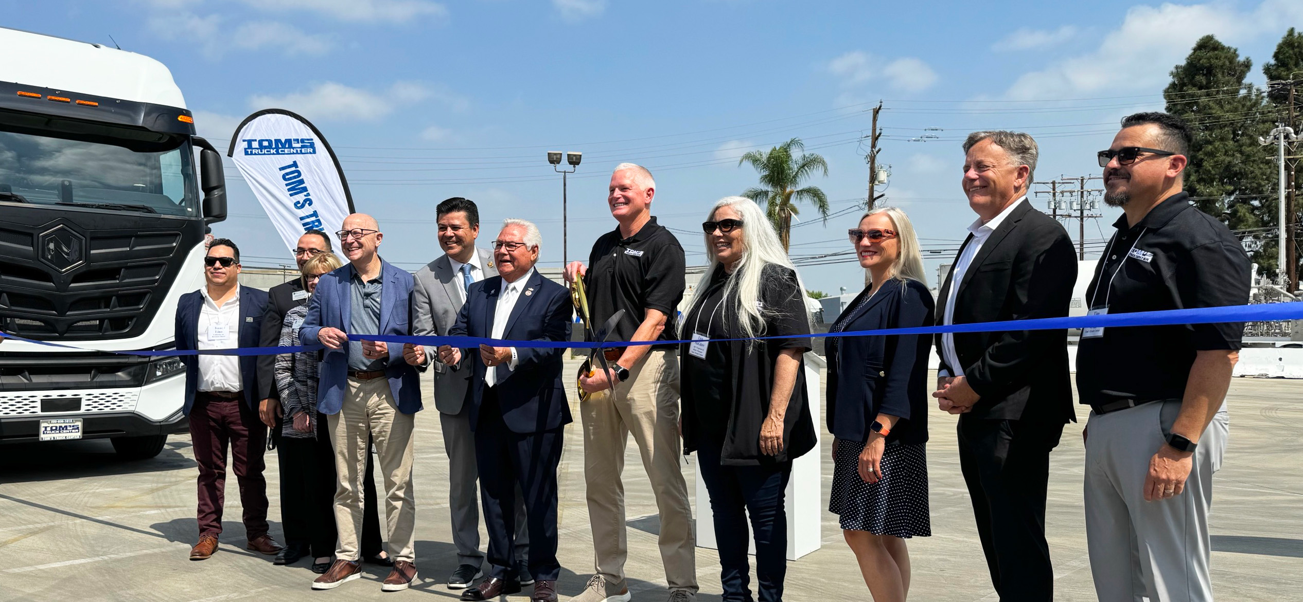 A group of people cutting a blue ribbon in front of a Nikola truck.