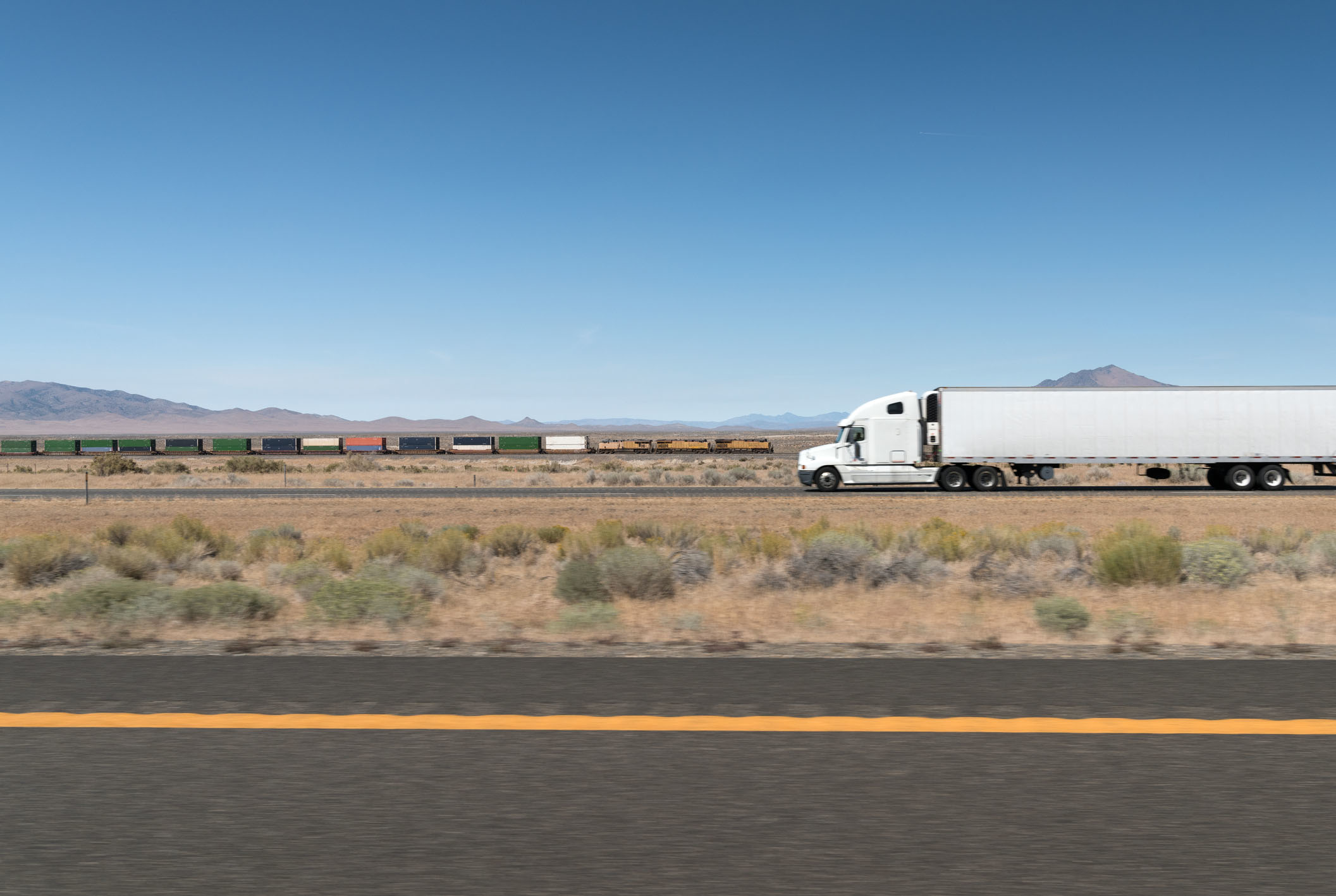 A truck and trailer drives on a highway in the desert.