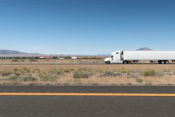 A truck and trailer drives on a highway in the desert.