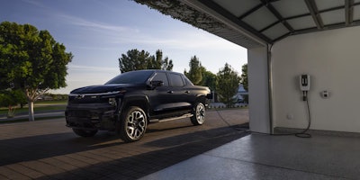 dark blue 2025 Chevy Silverado EV outside garage being charged by in-garage charger