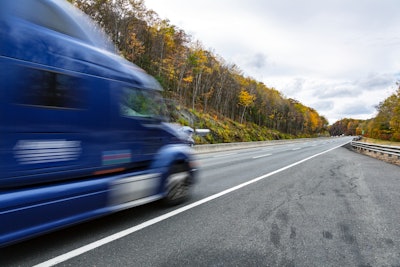 A blurry truck on a tree-lined road