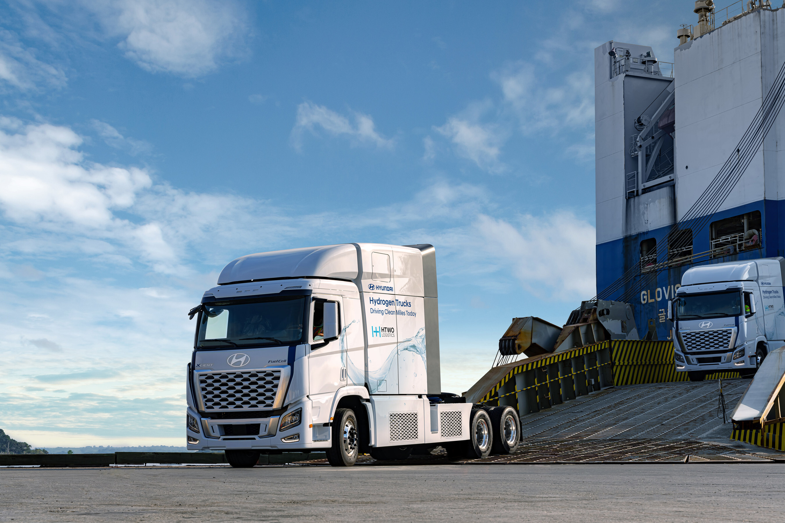 A Hyundai hydrogen fuel cell truck rolls down a ramp in front of a blue sky.