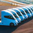 Fleet of blue and white semi-trucks parked in formation on an asphalt lot