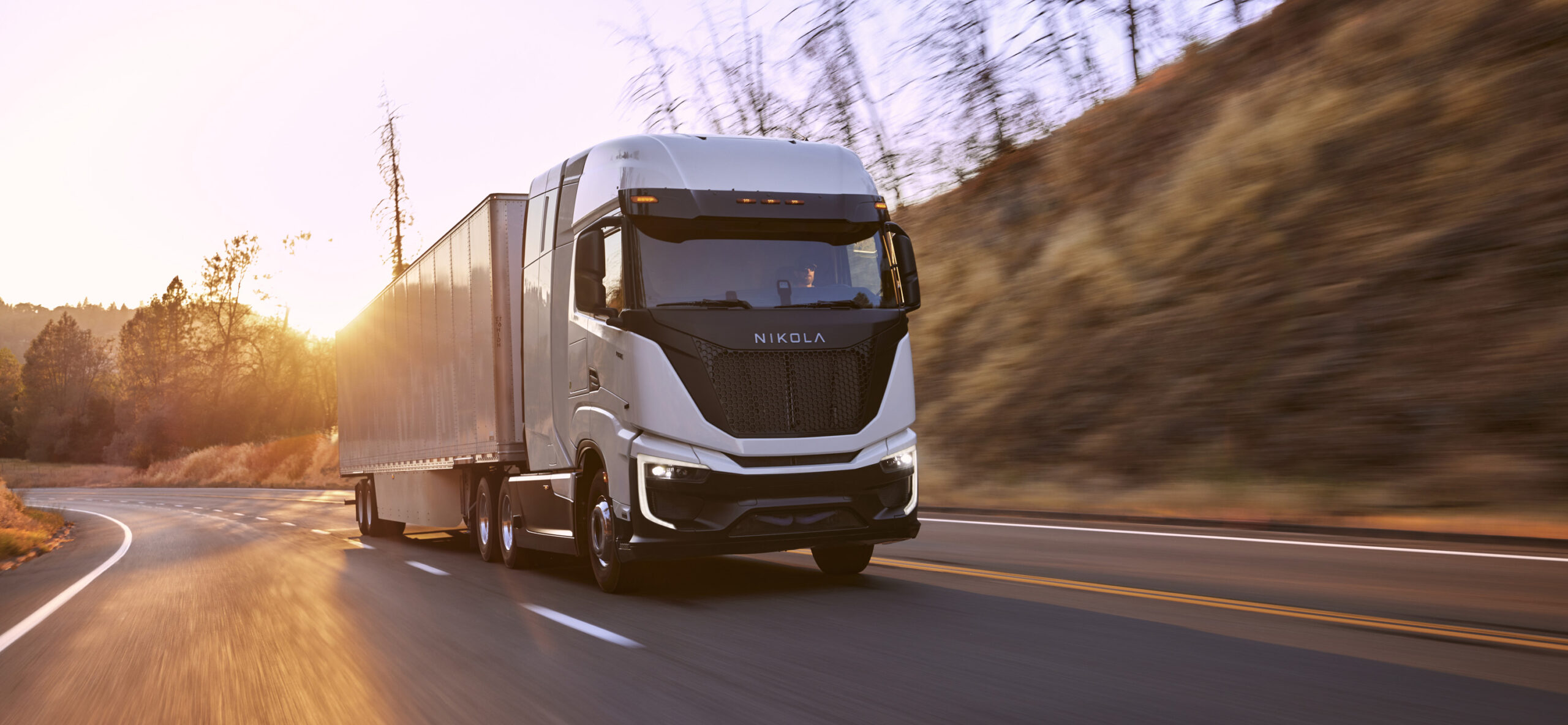 A Nikola Tre semi driving on a highway at sunset.