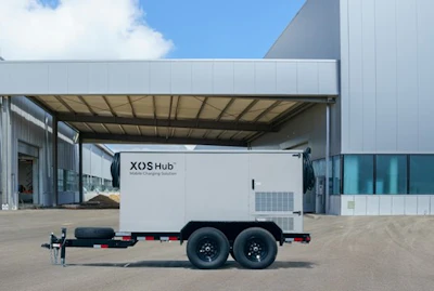White XOS Hub trailer parked near industrial building