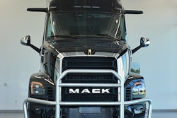 Black Mack semi-truck with chrome grille guard, front view in showroom