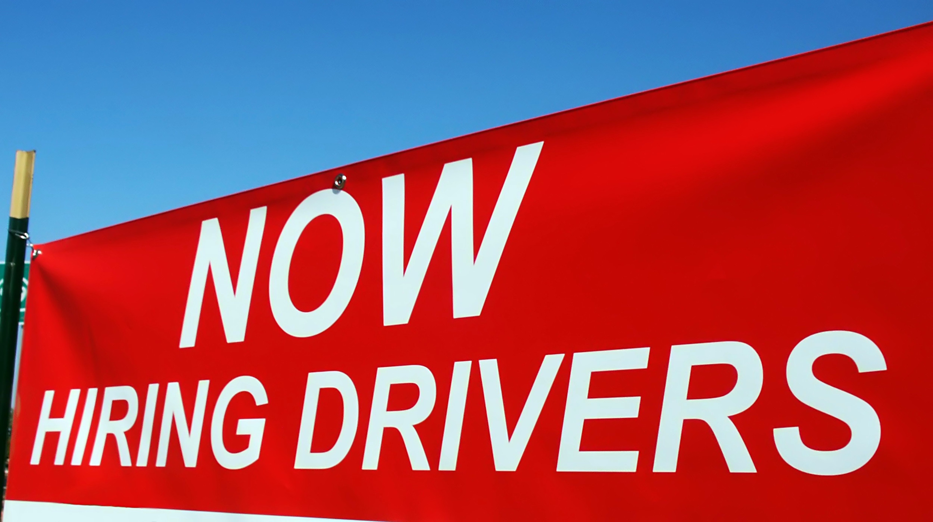Red hiring sign advertising job openings for drivers against blue sky