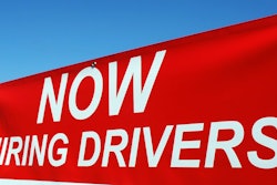 Red hiring sign advertising job openings for drivers against blue sky