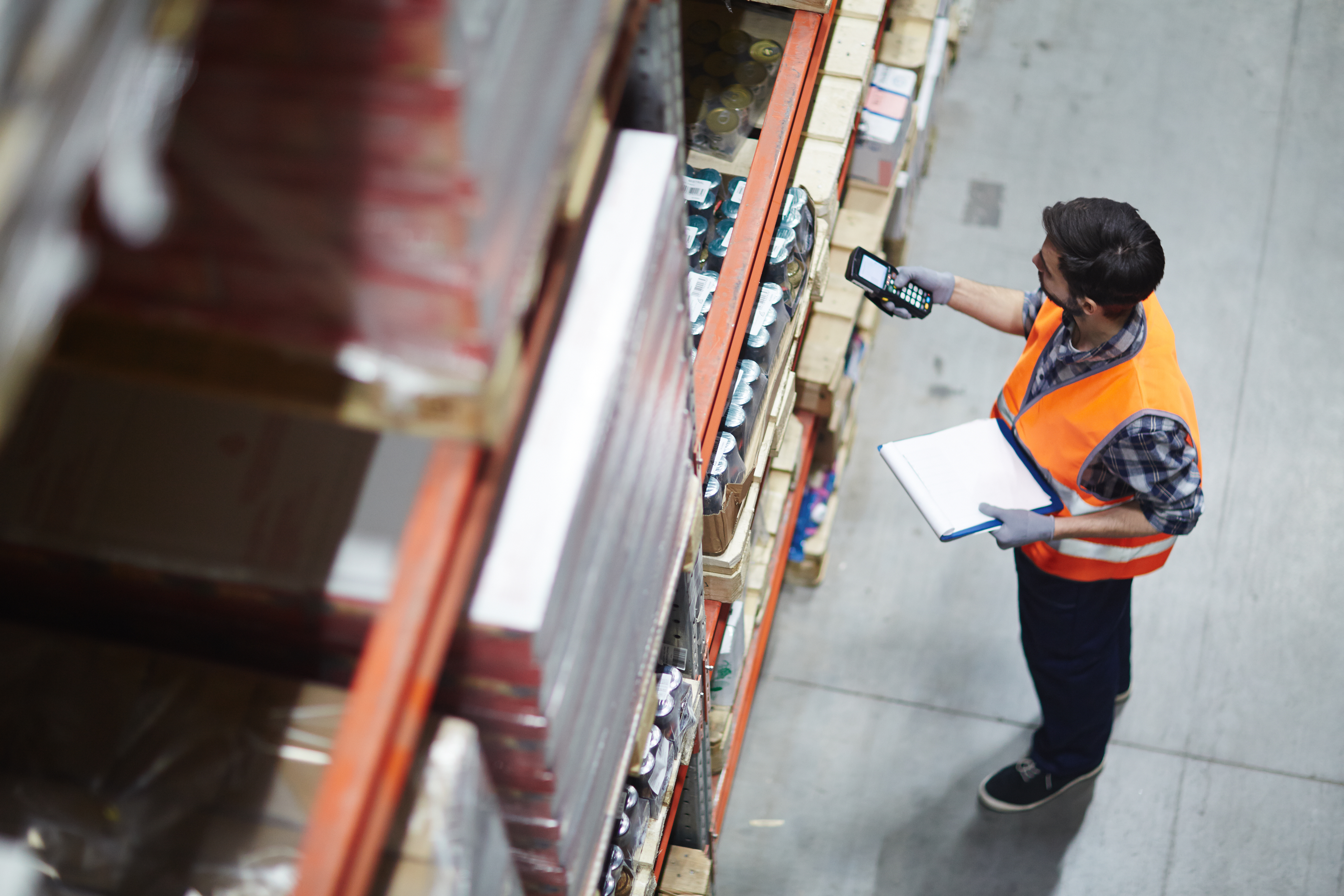 Warehouse worker in orange safety vest using scanner to check inventory on shelves