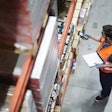 Warehouse worker in orange safety vest using scanner to check inventory on shelves