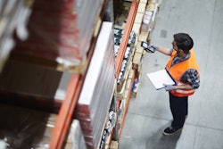 Warehouse worker in orange safety vest using scanner to check inventory on shelves