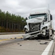 Damaged white semi-truck after highway collision, debris scattered on road