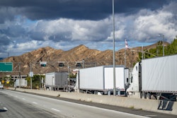 Line of big rig semi trucks with loaded semi trailers standing on the at the weighing station with scales for weighing along the axes.