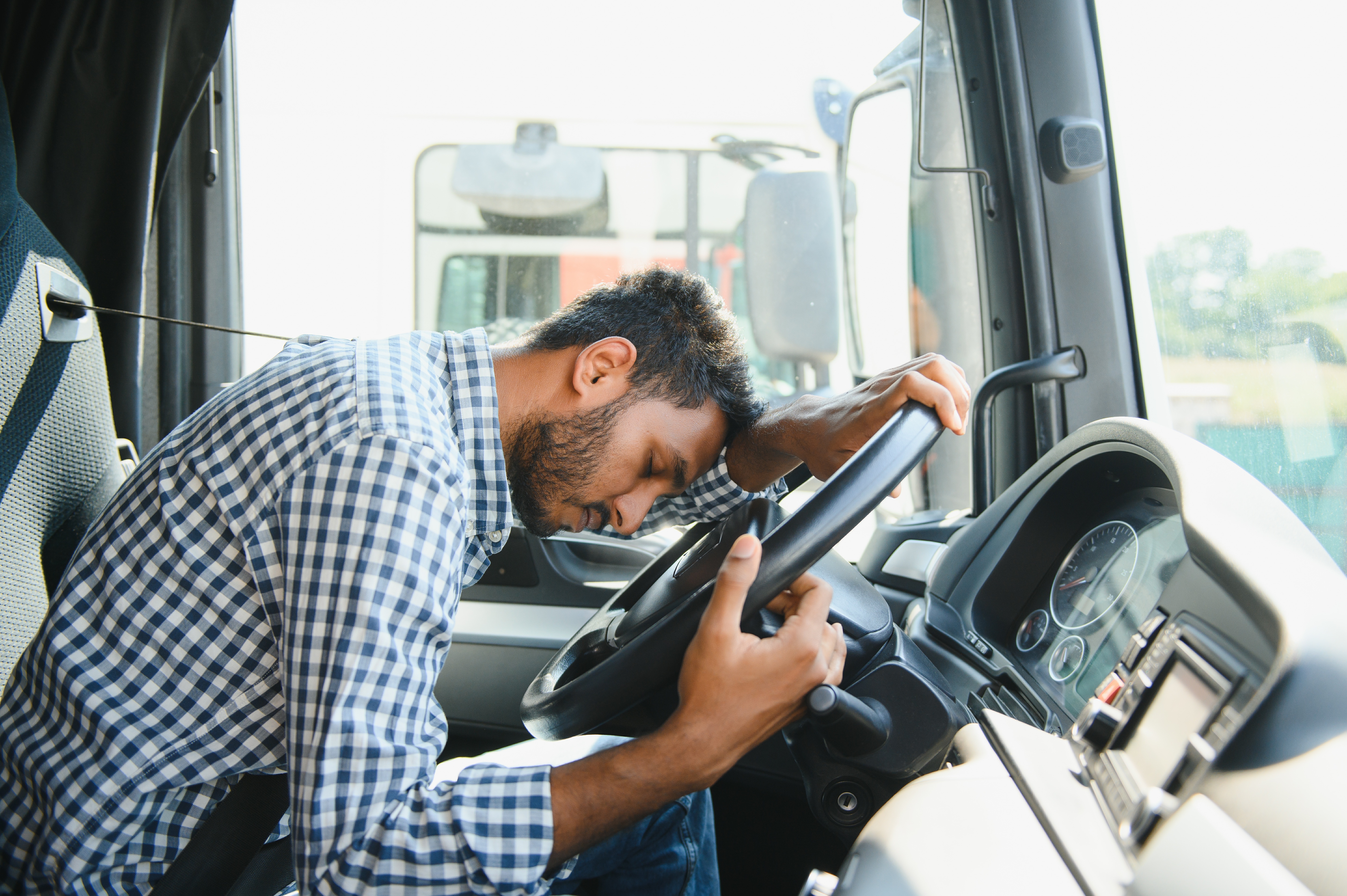 Truck driver asleep at steering wheel in blue checkered shirt