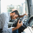 Truck driver asleep at steering wheel in blue checkered shirt