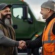 Two workers in safety vests shaking hands near a green truck