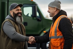 Two workers in safety vests shaking hands near a green truck